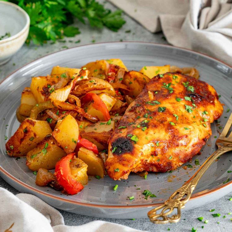 Golden honey garlic chicken breast served with roasted potato chunks, bell peppers, and caramelized onions, sprinkled with chopped parsley.
