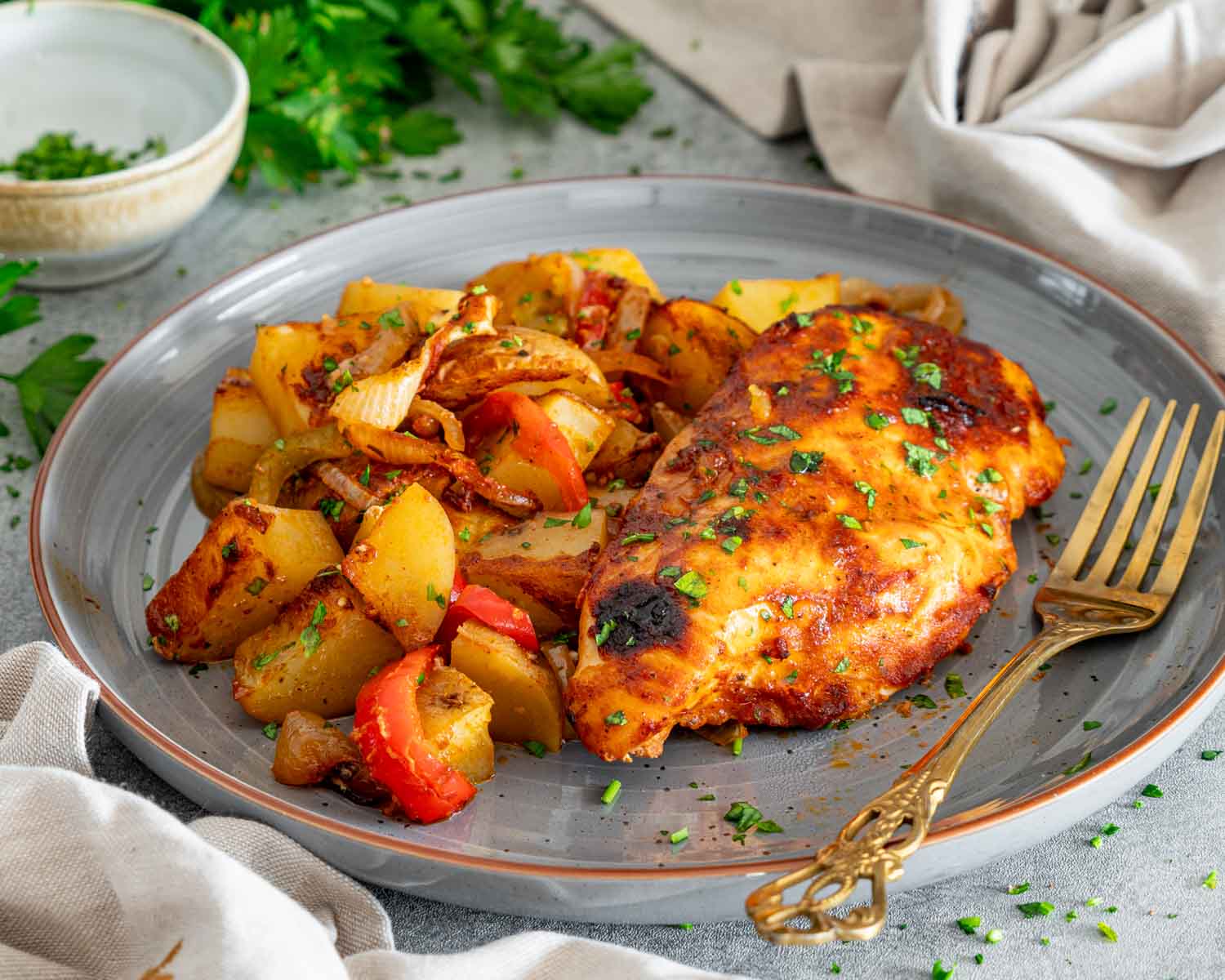 Golden honey garlic chicken breast served with roasted potato chunks, bell peppers, and caramelized onions, sprinkled with chopped parsley.